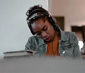 A woman writing at a table with headphones on
